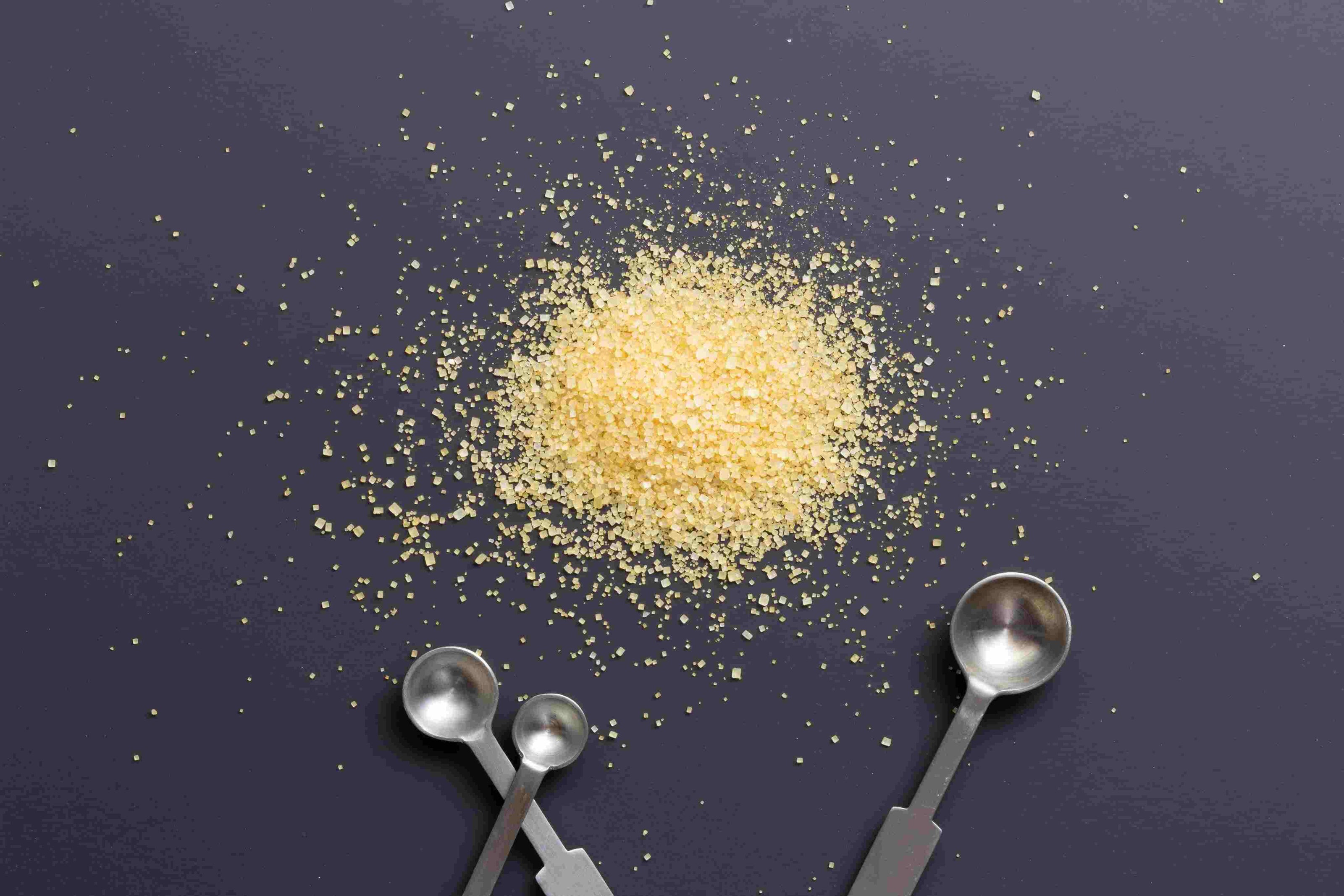 3 measuring spoons laying beneath a mound of raw sugar crystals.